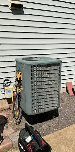 A sun-faded green outdoor AC unit with tools next to a house with siding