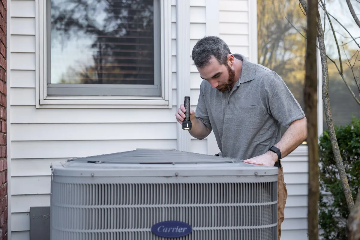 Technician inspecting a residential outdoor air conditioning condenser with a flashlight