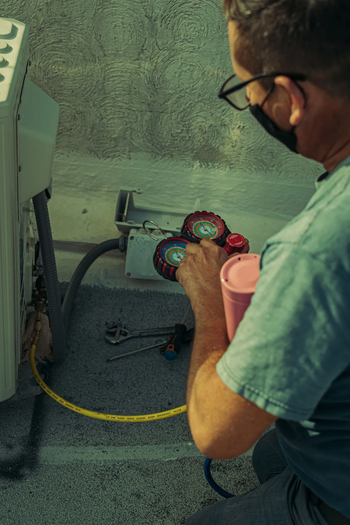 Technician servicing an outdoor air conditioning unit with manifold gauges