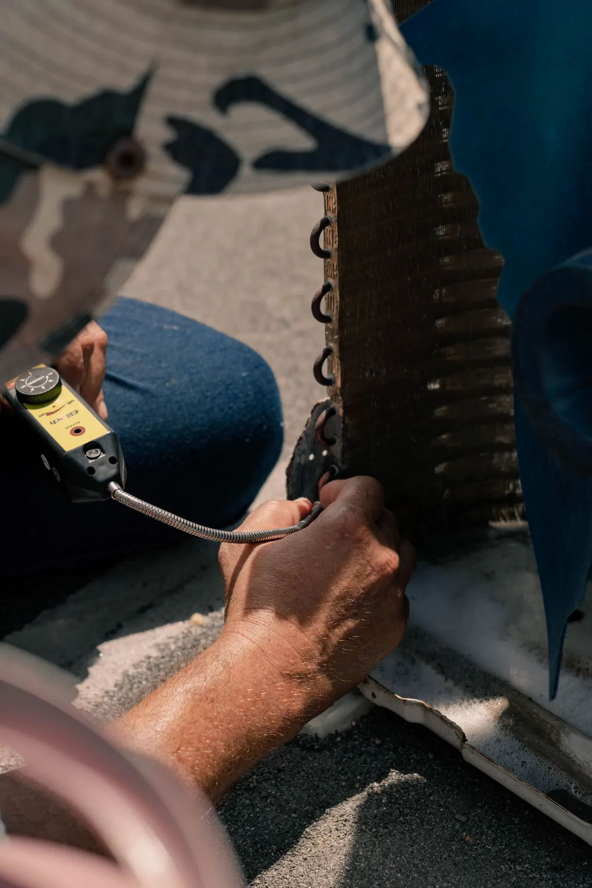 Technician using a hand-held meter beside an air conditioning condenser's coil fins