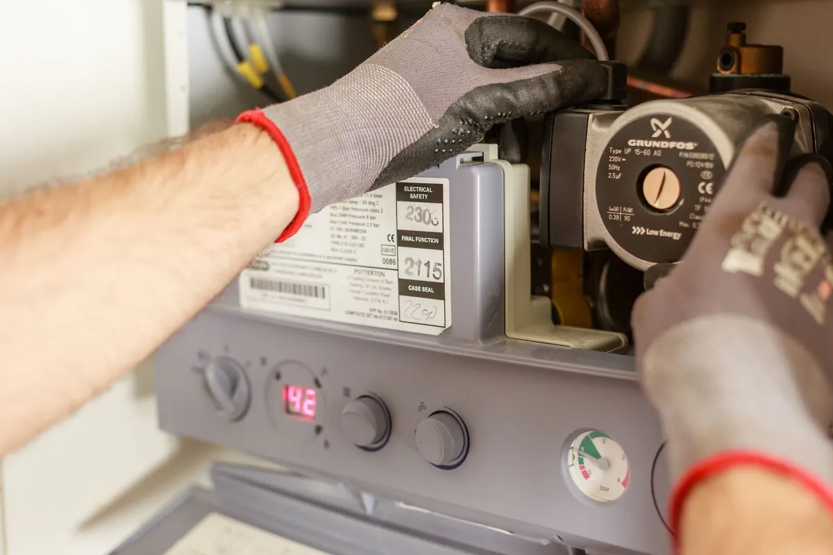 Technician's hands working inside a wall-mounted boiler beside its circulation pump