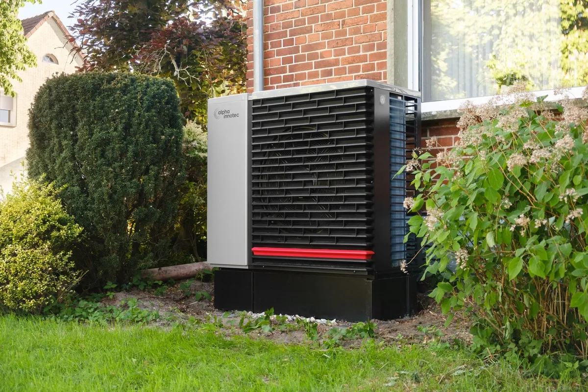 Residential heat pump unit standing in a garden beside a brick house