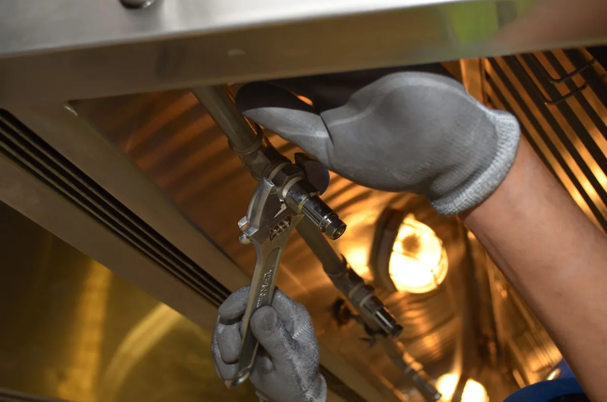 Gloved hands using a wrench inside a heating appliance with the burner visible