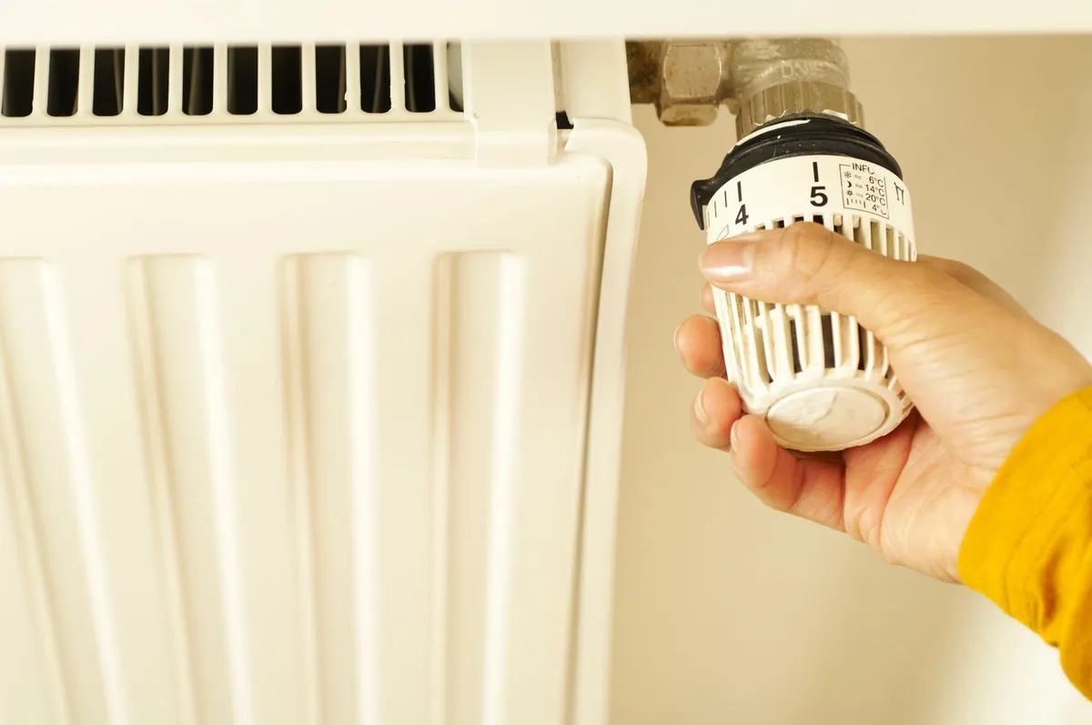 Hand adjusting the thermostatic valve on a radiator