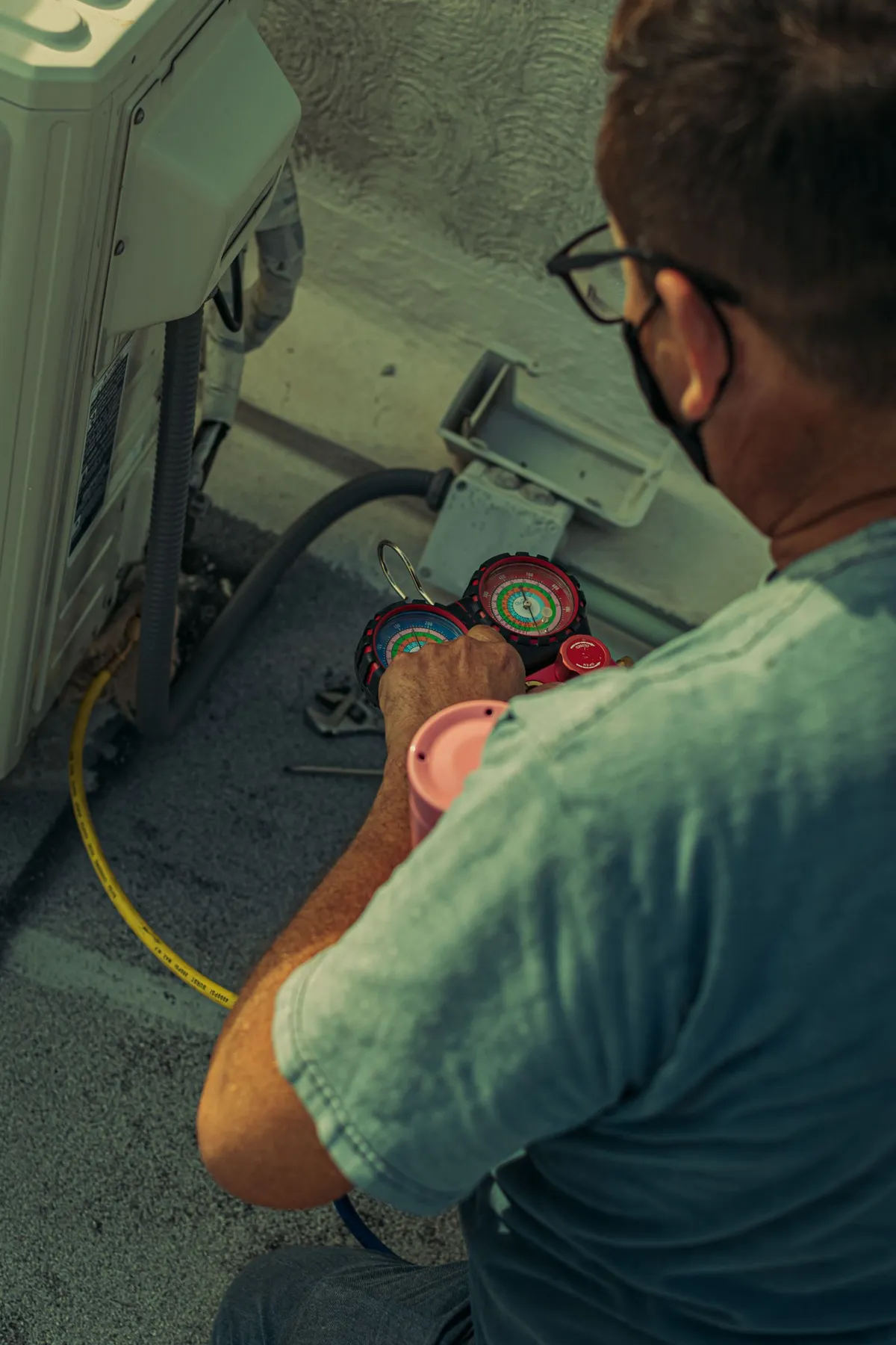 Technician checking refrigerant pressures on an outdoor HVAC unit