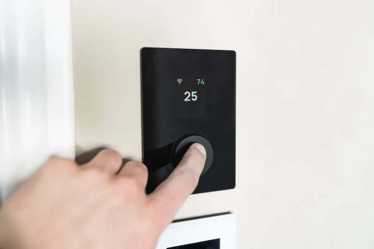 Finger pressing the dial of a wall-mounted smart thermostat